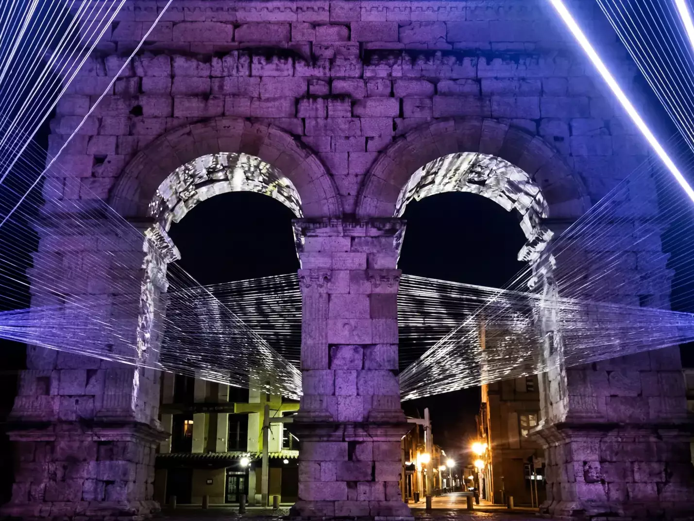 Arc Germanicus de Saintes illuminé de nuit pour la célébration de ses 2000 ans, avec scénographie lumineuse violette et faisceaux artistiques autour du monument antique.