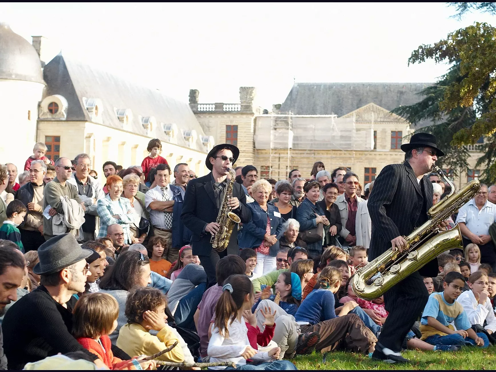 Deux musiciens saxophonistes jouent au cœur d’un public familial rassemblé devant un château lors du spectacle Fanf’Oiron.