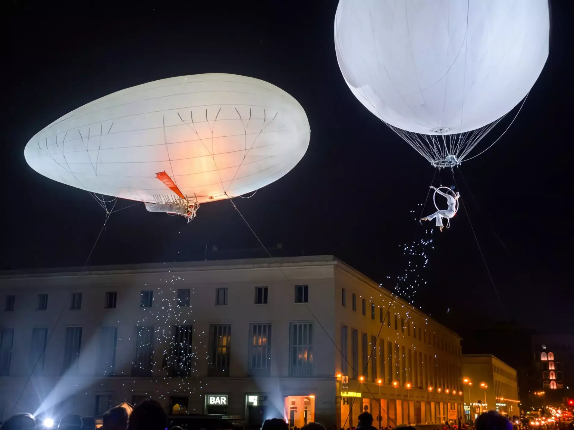 Deux grands ballons lumineux survolent la ville de nuit avec des artistes aériens suspendus, jeux de lumière et public rassemblé pour le spectacle Jour de Loire.