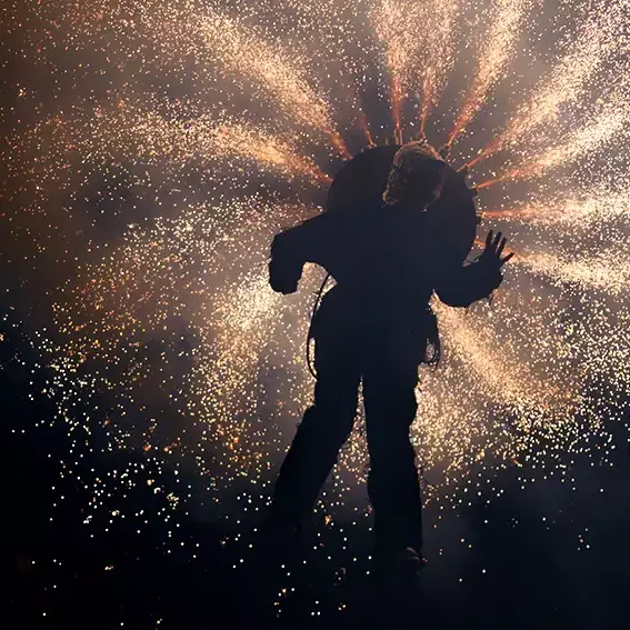 Spectacle pyrotechnique nocturne des Nuits Romanes avec artiste en silhouette devant une pluie d’étincelles lumineuses.