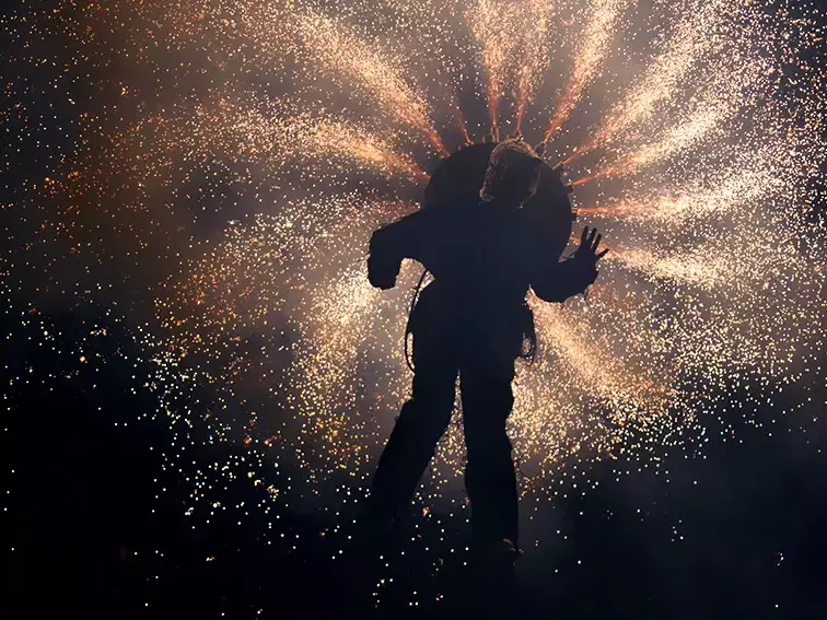 Spectacle pyrotechnique nocturne des Nuits Romanes avec artiste en silhouette devant une pluie d’étincelles lumineuses.