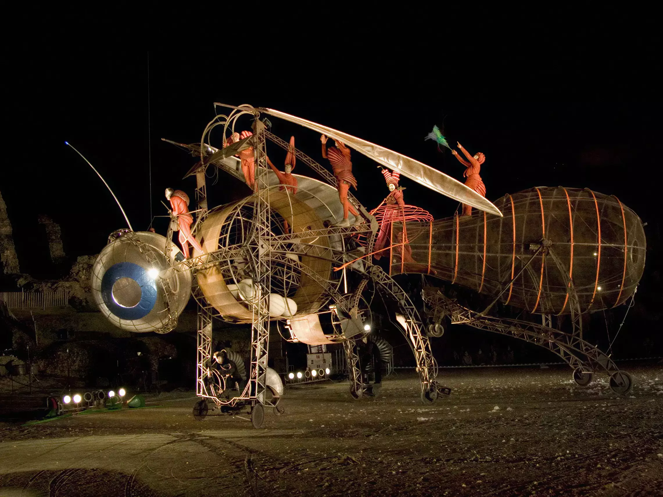 Spectacle de rue nocturne avec machine artistique géante, acrobates et scénographie mécanique en plein air.