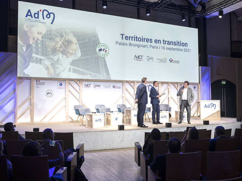 Événement professionnel Ademe au Palais Brongniart à Paris, avec intervenants sur scène, public en salle et projection grand format pour la conférence Territoires en transition.