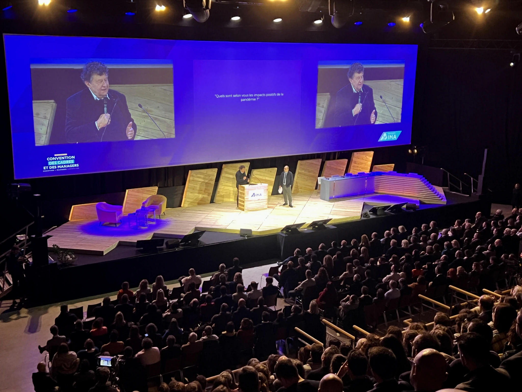 Conférence professionnelle du Groupe IMA en auditorium, avec intervenants sur scène, projection vidéo grand format, décor en bois et public nombreux pour la convention des cadres et managers.