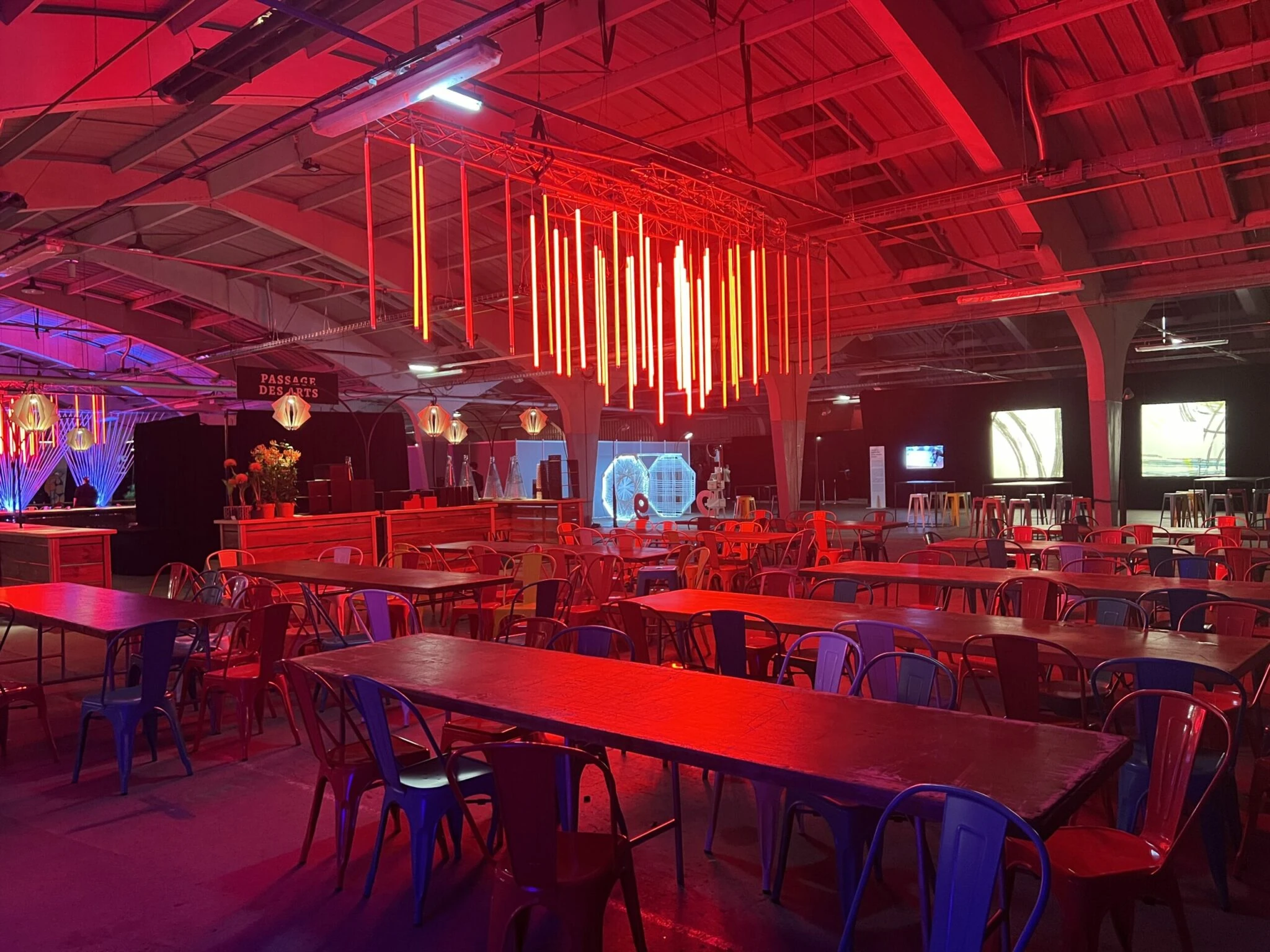 Scénographie événementielle pour les 90 ans de la MAIF avec éclairage rouge, tables de réception et installations lumineuses suspendues.