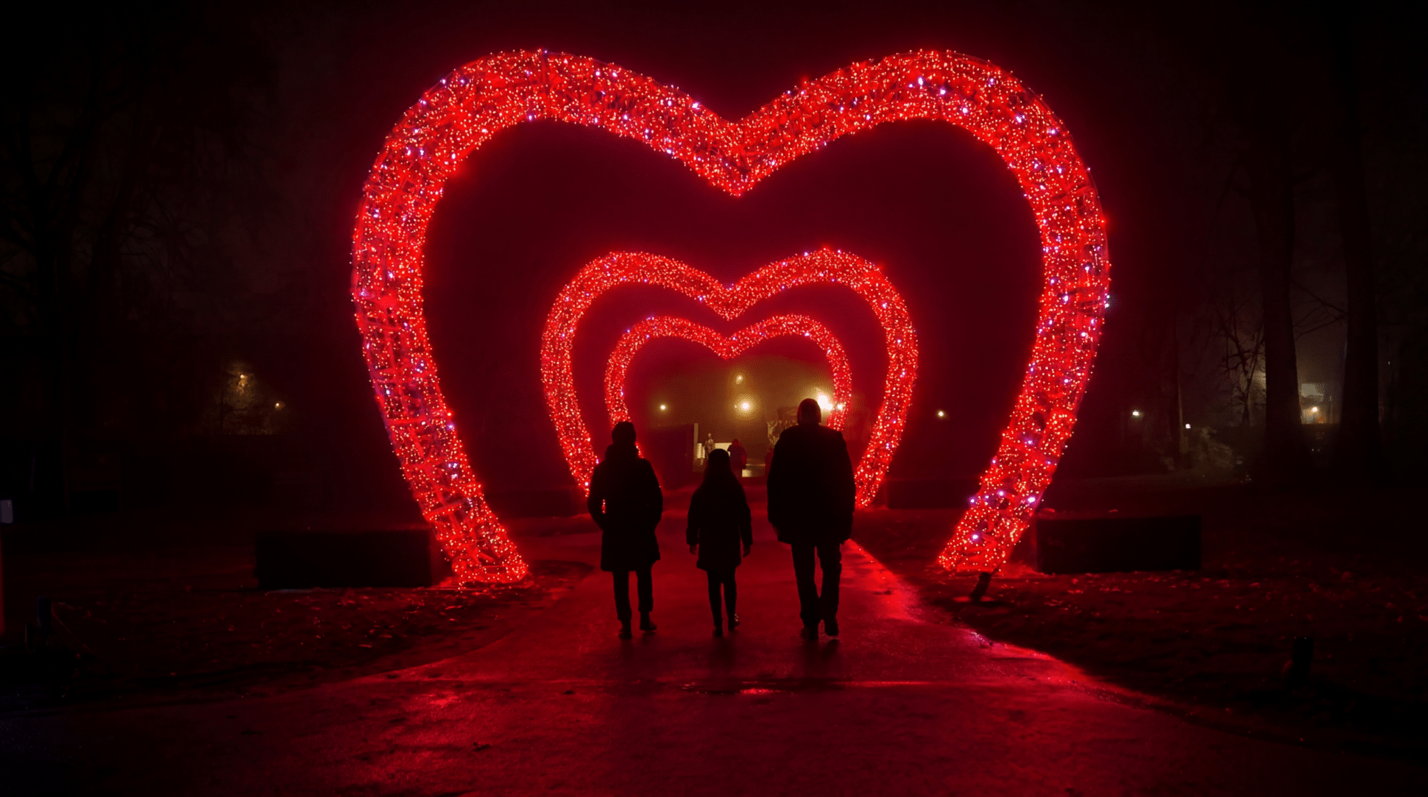 3 grands cœurs lumineux rouges illuminés la nuit dans le parc de l'Abbaye de l'Épau, avec trois visiteurs passant dessous