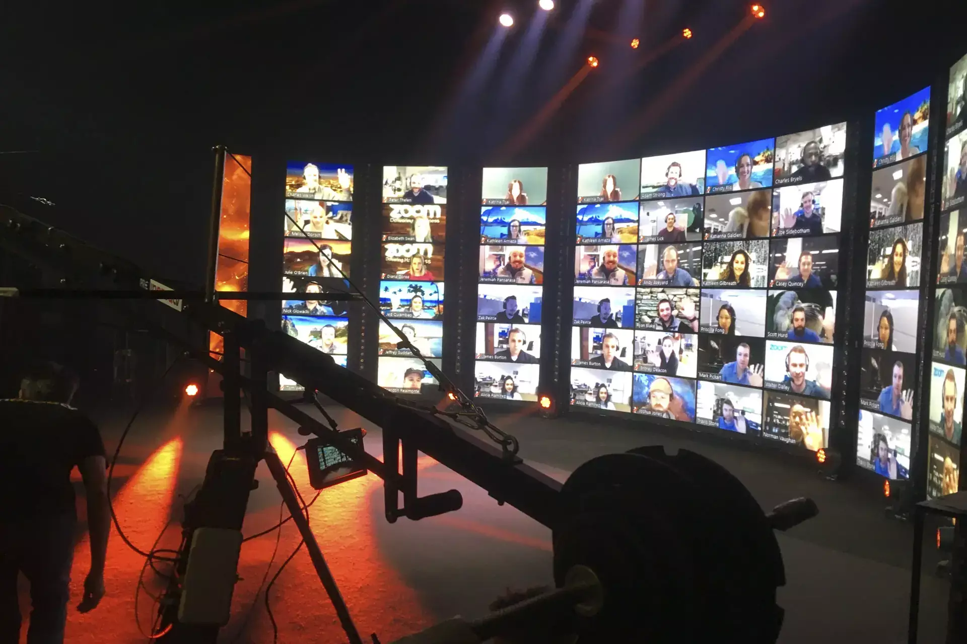 Tournage d’un événement hybride sur plateau avec caméra grue, mur vidéo affichant des participants en visioconférence Zoom et mise en lumière scénique professionnelle.