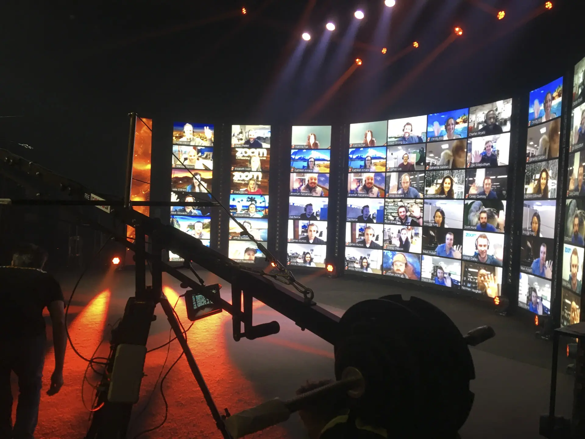 Tournage d’un événement hybride sur plateau avec caméra grue, mur vidéo affichant des participants en visioconférence Zoom et mise en lumière scénique professionnelle.